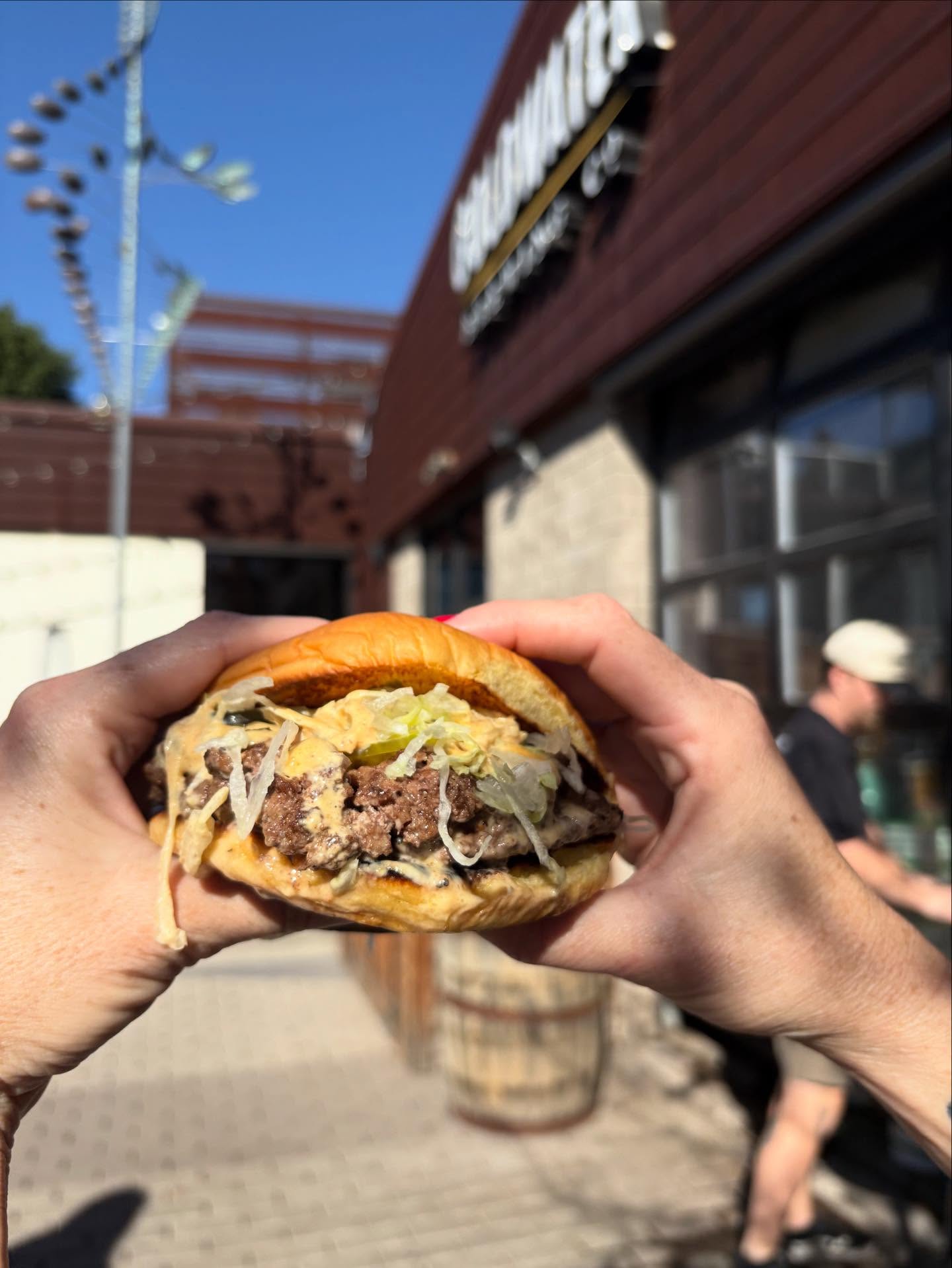 Grass-fed smash burger with grilled onions and spicy sauce outside a brewery